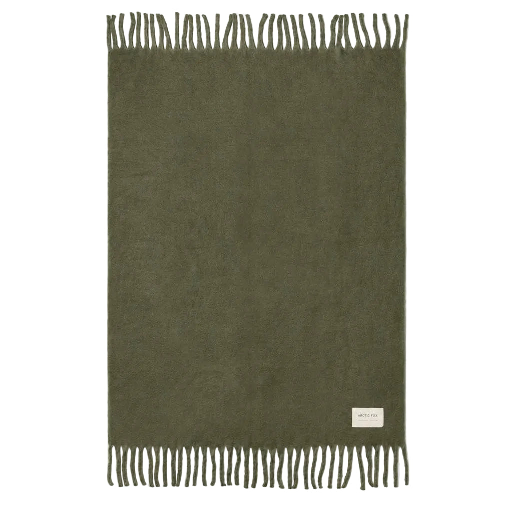 An olive green rectangular throw with fringed edges and a small white brand label near the bottom right, displayed flat against a light off-white background.