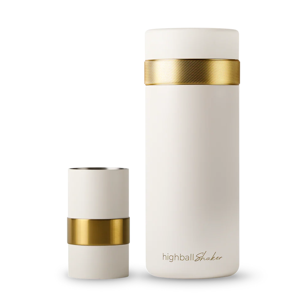 An off-white insulated bottle with a textured gold band and a matching off-white cap, shown on a clean white background. The shot glass is placed beside the shaker.