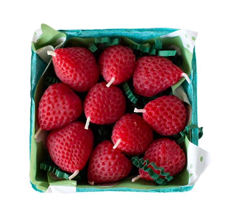 Handmade strawberry-shaped beeswax candles sit in a paper berry basket with leafy filler. Perfect for birthdays or table decor.