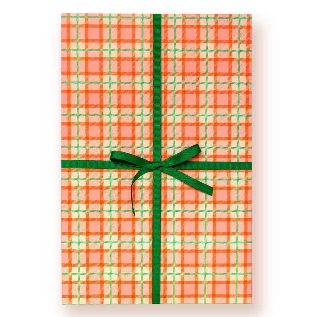 Orange and light green plaid wrapping paper on a giftbox tied with a dark green ribbon and bow, on a white background