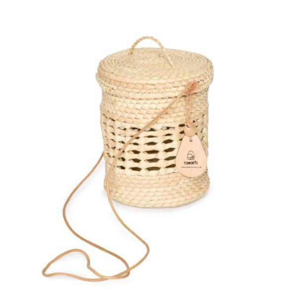 Lantern Canasta round basket bag with structured body, leather cord strap, and attached circular lid. Perfect for beach days or daily use.