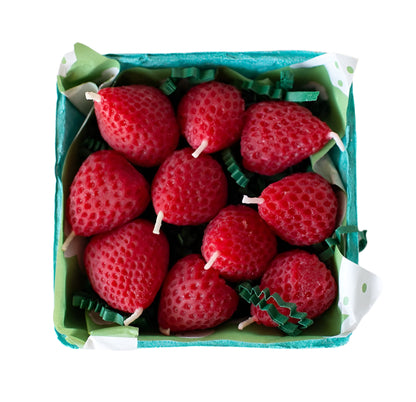 Handmade strawberry-shaped beeswax candles sit in a paper berry basket with leafy filler. Perfect for birthdays or table decor.