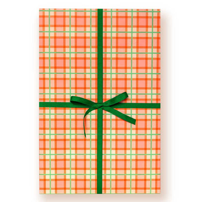 Orange and light green plaid wrapping paper on a giftbox tied with a dark green ribbon and bow, on a white background