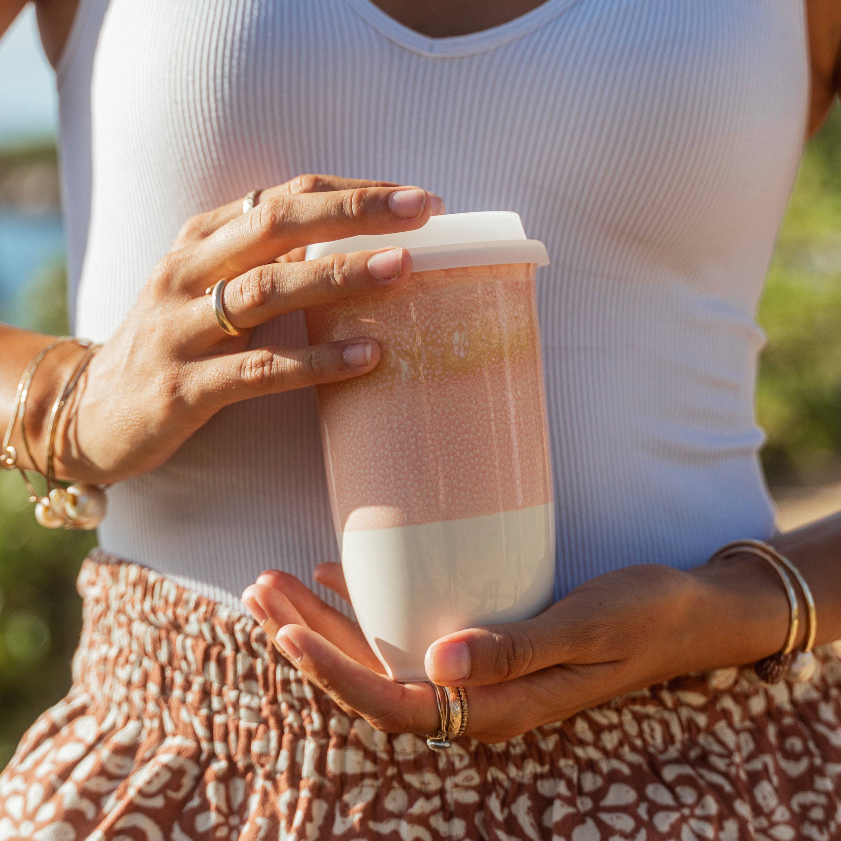 Person holding a pink and white reusable cup outdoors