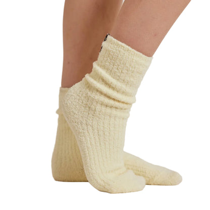 A close-up of a person's feet wearing a pair of pale cream-colored, textured crew socks against a white background.
