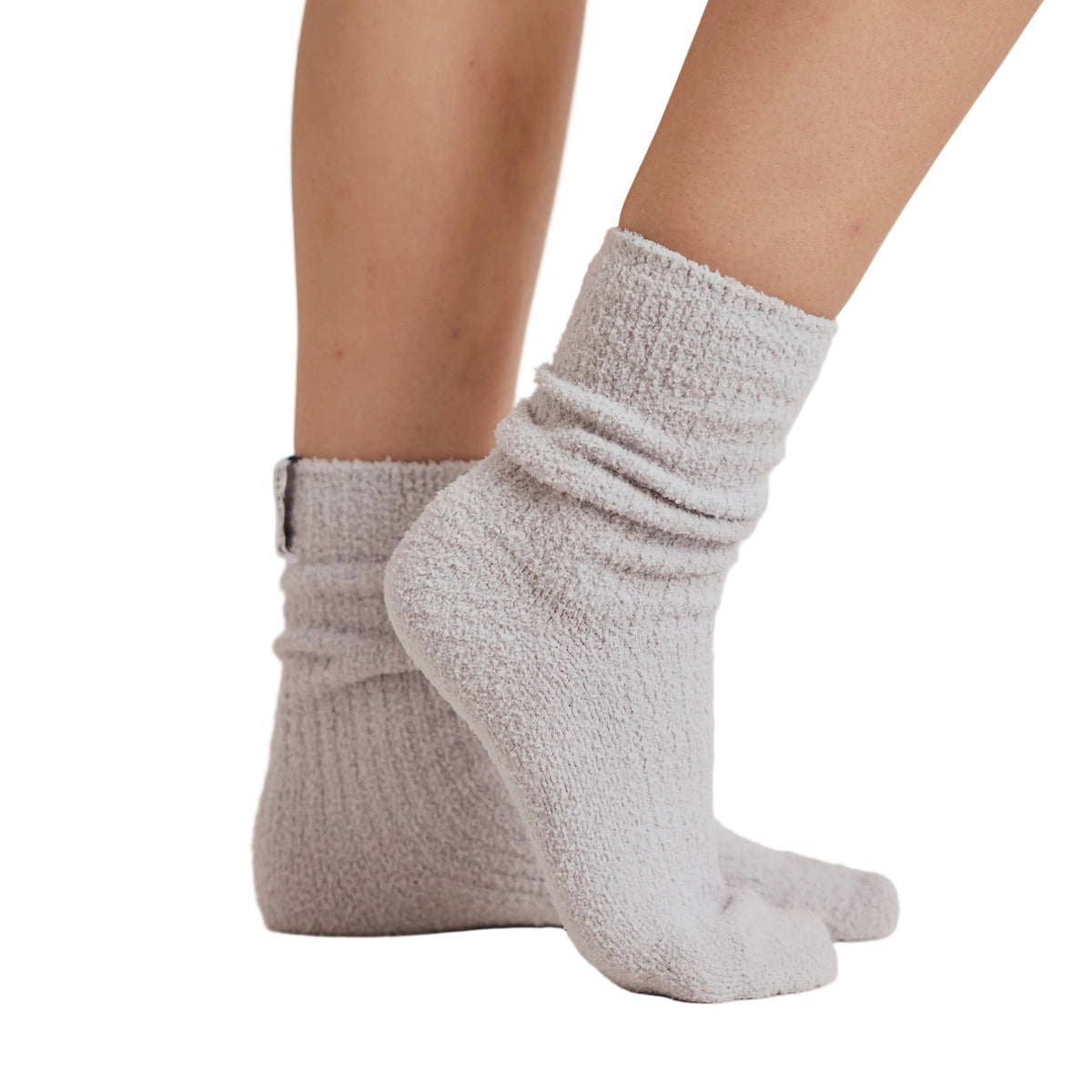 A close-up of a person's feet and lower legs wearing light gray ribbed ankle socks, standing against a white studio background.