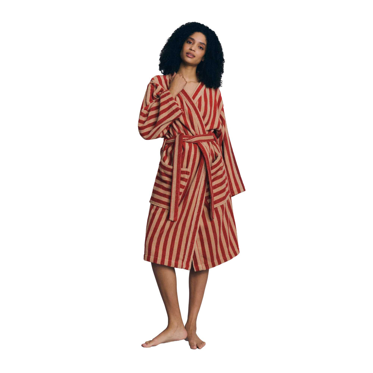 A woman modeling a long-sleeved, belted robe with vertical red and beige stripes, standing against a solid white background.