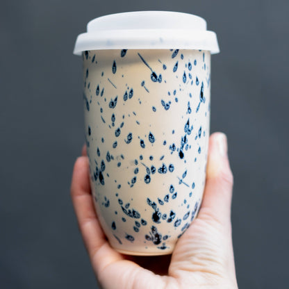 Hand holding a paper cup with blue speckled design against a dark background