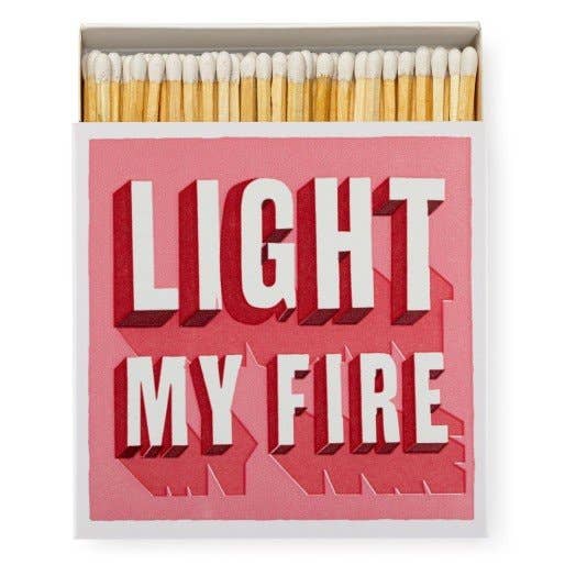 Retro pink matchbox with bold red-and-white 'Light My Fire' typography, filled with long strike-on-box matches