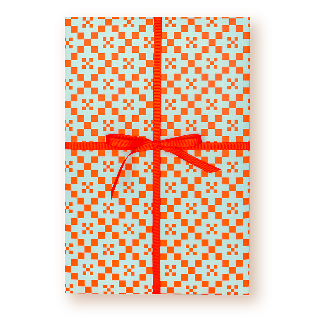 A rectangular gift box wrapped in light blue wrapping paper with a bright orange geometric checkered pattern and tied with a red ribbon and bow, shown on a white background.