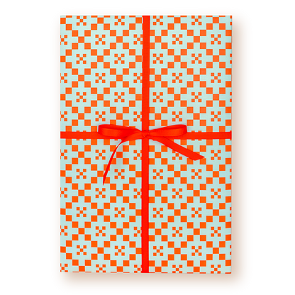 A rectangular gift box wrapped in light blue wrapping paper with a bright orange geometric checkered pattern and tied with a red ribbon and bow, shown on a white background.