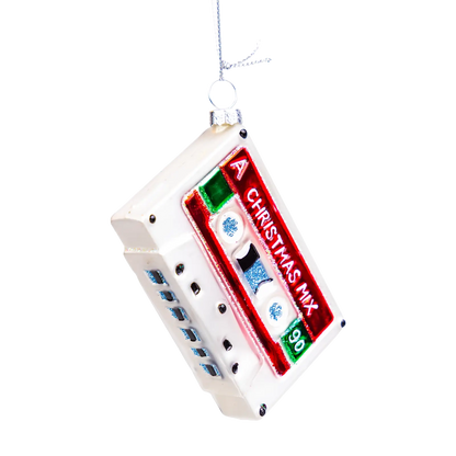 A Christmas ornament shaped like a retro cassette tape, featuring a white plastic body with a red label that reads 'CHRISTMAS MIX 96' and small blue and green details, hanging from a silver string against a white background.