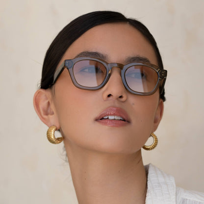 Person wearing glasses and gold hoop earrings with a neutral background