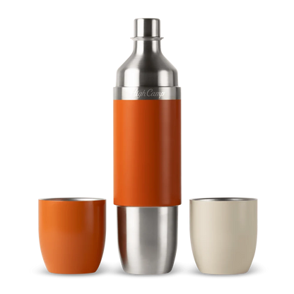 A stainless steel cocktail shaker with an orange sleeve, shown with two tumblers on a white background. One tumbler is orange and the other is a light cream color.